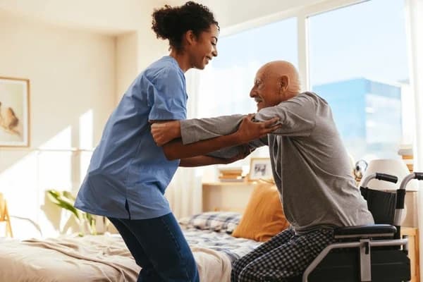 A caregiver helping an older adult rise safely from a wheelchair